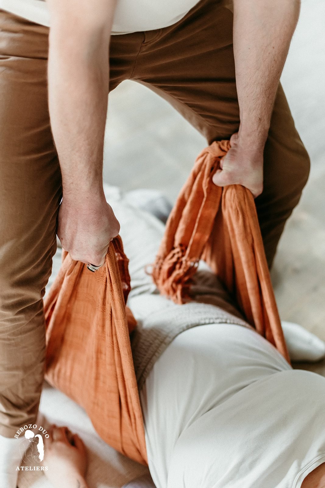 Soin Slow Rebozo : un tissu terracotta enveloppe le bassin d'une femme allongée